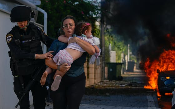 警察官に誘導され、子どもを抱いて避難する女性（7日、イスラエル中部アシュケロン）=AP